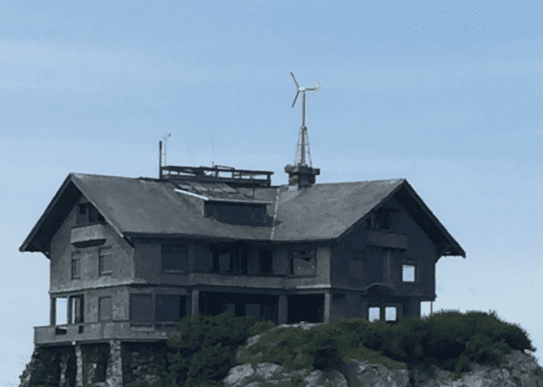 Frame 1618873797 A large wooden house with a wind turbine on top of it.